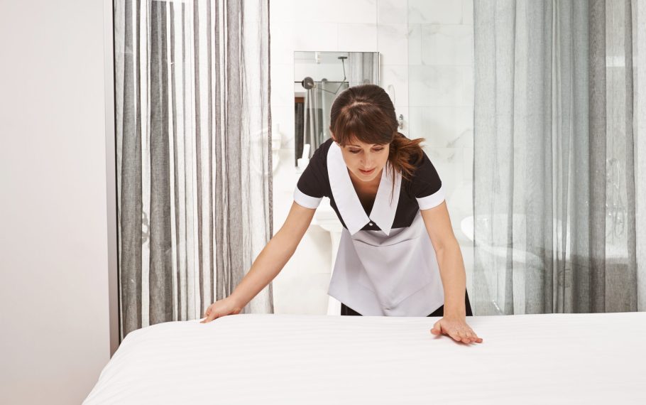 Woman in maid uniform making bed. Portrait of female housecleaner putting on new blankets and clean hotel room, trying her best not to miss any spot and let visitors enjoy their stay in nice place Hotel cleaning services